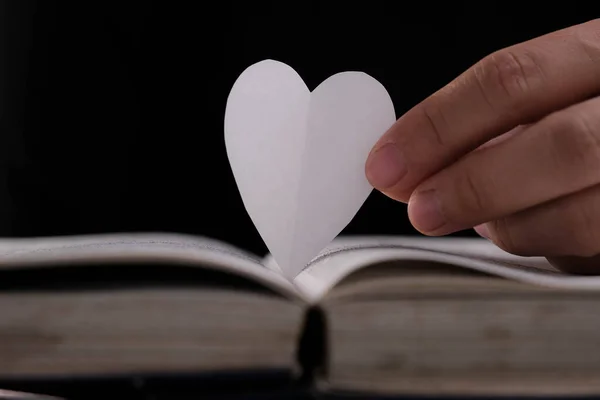 Book with open pages and heart shaped paper. Woman hand holding heart shaped paper over open book on table. love of reading concept