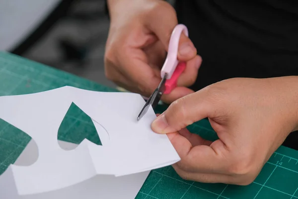 Bir kadın süslemek için beyaz kalp şeklinde bir kağıdı makasla keser. Sevgililer Günü tebrik kartı ya da bayram hediyesi konsepti.