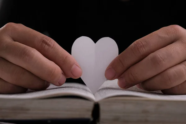 Book with open pages and heart shaped paper. Woman hand holding heart shaped paper over open book on table. love of reading concept