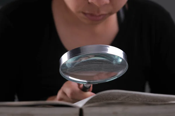 教科書の虫眼鏡を通して見ている女性のクローズアップ 手でガラスを拡大し テーブルの上に本を開きます 研究の概念 — ストック写真