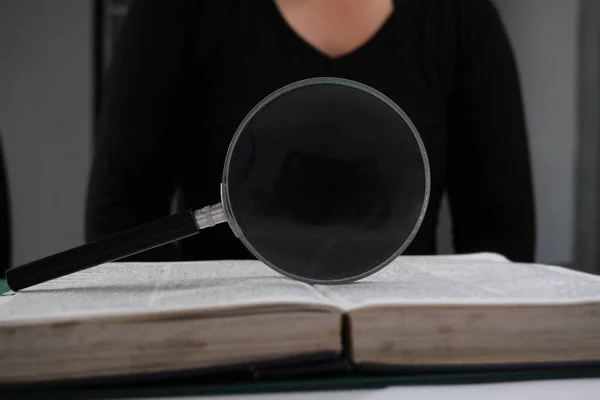 Magnifying glass over open book on table. Education and research concept.