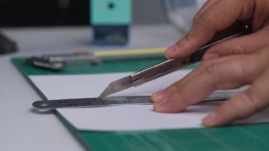 Bıçak makası ile kağıt kesen kadınların yakın çekim elleri. Bıçaklı kadın eli paspasın üzerinde cetvelle kağıt kesiyor..