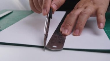 Bıçak makası ile kağıt kesen kadınların yakın çekim elleri. Bıçaklı kadın eli paspasın üzerinde cetvelle kağıt kesiyor..