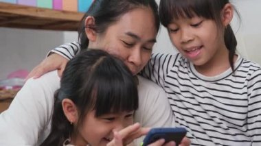 Anne ve kız oynuyor, sarılıyor, akıllı telefonlarda selfie çekiyor, çizgi film izliyor ya da evde online oyunlar oynuyor. Mutlu aile ve Anneler Günü konsepti.