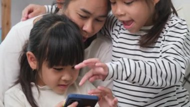 Anne ve kız oynuyor, sarılıyor, akıllı telefonlarda selfie çekiyor, çizgi film izliyor ya da evde online oyunlar oynuyor. Mutlu aile ve Anneler Günü konsepti.