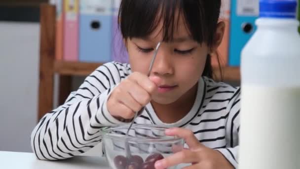 小さな女の子はリビングルームで自宅で新鮮な赤ブドウを食べる かわいい若いアジアの女の子は彼女の食事のために健康的な果物やミルクを食べる 子供の頃の健康食品 — ストック動画