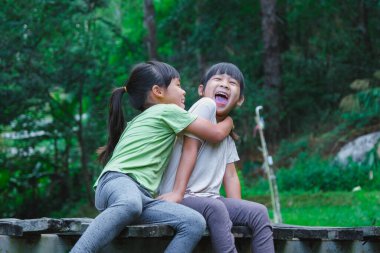 Güzel Asyalı kızlar ahşap köprüde birlikte oturuyorlar. İki mutlu genç kız dışarıda eğleniyor. Bahçede oynayan Asyalı kardeşler.