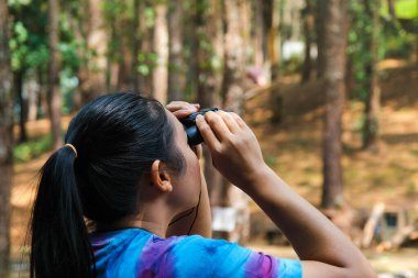 Ormandaki kuşlara dürbünle bakan genç bir kadın. Ormanda doğayı izleyen aletli bir kadın turist. Sağlıklı yaşam tarzı ve eko-turizm.