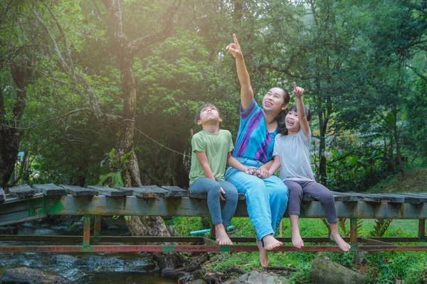 快乐的年轻妈妈和小女孩坐在河边的木桥上 妈妈和两个女儿在户外玩的很开心 母亲节快乐温馨的家庭 — 图库照片