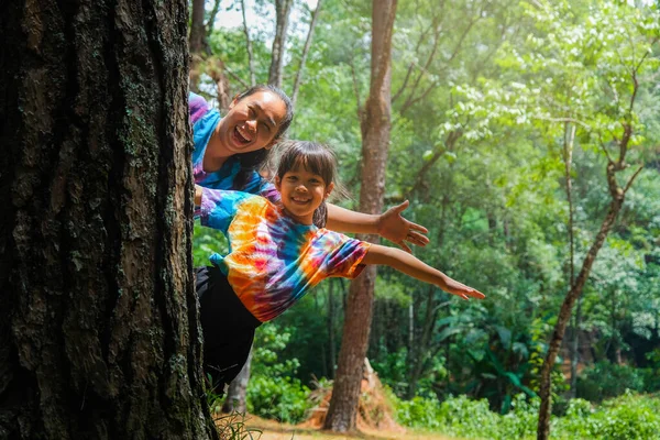 快乐的家人躲在树后 在公园里玩耍 快乐的母亲和女儿躲在树干后面绿色环保生活方式 爱与保护自然的概念 — 图库照片