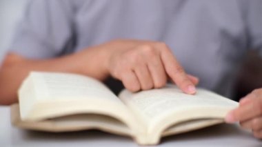 Asyalı bir kadının masa başında oturmuş oturma odasında kitap okuduğu yakın plan..