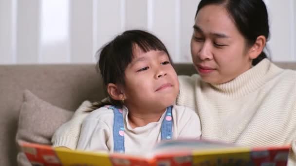 妈妈和女儿在家里的沙发上看书 快乐的母亲读书 给孩子们讲有趣的故事以及在家里共度时光 — 图库视频影像