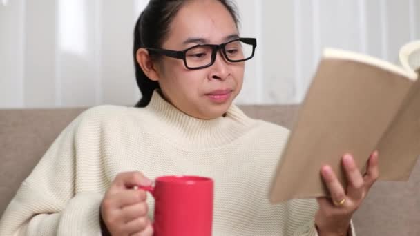 Szczęśliwa Młoda Kobieta Trzymająca Filiżankę Kawy Czytająca Książkę Kanapie Obudzeniu — Wideo stockowe