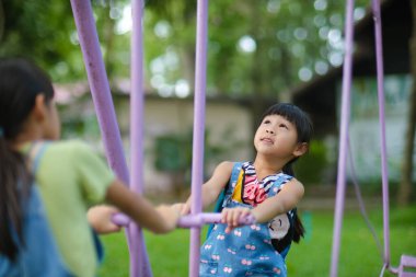 İki tatlı kız kardeş yaz boyunca oyun alanında oynarken eğleniyorlar. Sevimli küçük bir kız, gülücükler saçarak bir parkta at sallıyor. Çocuklar için aktif yaz tatili.