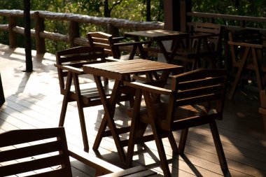 Parktaki açık kafe terasında tahta masalar ve sandalyeler. Yeşil bahçeyle çevrili boş bahçe mobilyaları.
