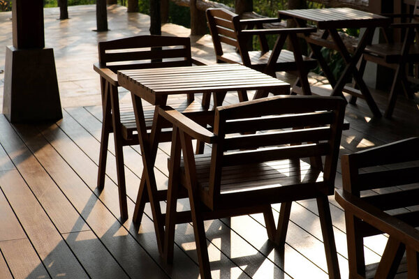 Wooden tables and chairs at outdoor cafe terrace in park. Empty garden furniture surrounded by green garden.