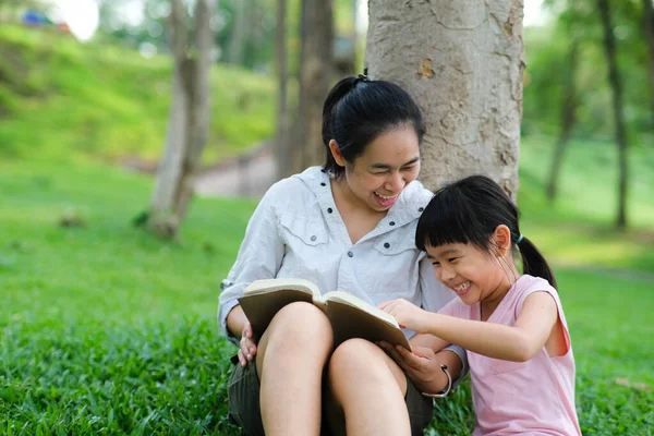 Happy mother and little girl having fun and enjoying reading at the park. Mother and daughter resting in the summer garden, she reads fairy tales to her daughter.