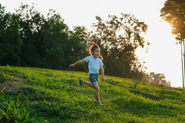 夏の公園で草の上を走っている幸せな少女 夕日の光で草原を駆け抜ける少女 — ストック写真