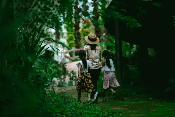 可爱的女儿和母亲手牵着手走在植物园的石道上 周围种满了绿色的植物和五彩缤纷的花朵 — 图库照片