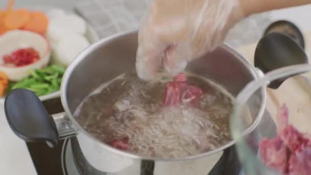 シェフの手は 台所で沸騰した水の鍋に豚の肋骨を入れています 鍋に野菜 スープ と豚肉ストックを準備します 自家製ブイヨンレシピ — ストック動画
