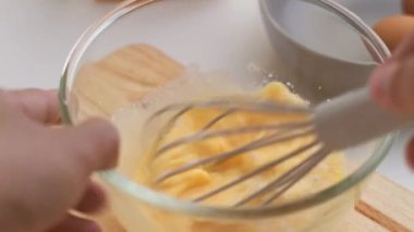 Kadın cam kasede yumurta çırpıyor. Genç bir kadın mutfakta yemek pişiriyor..