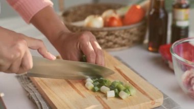 Negi 'yi (Japon Uzun Soğanı), Japon Scallion' u ya da tahta kesme tahtasındaki yeşil soğanı kesmek için bıçak kullanan bir kadın. Kadın evde yemek hazırlıyor..