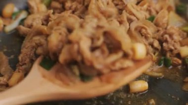 Mutfaktaki tavada kepçeyle kızartılmış kimchi ve kurobuta domuz eti tutan eller. Öğle yemeği için Kore ev yemeği.