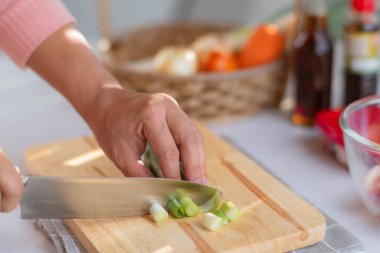 Negi 'yi (Japon Uzun Soğanı), Japon Scallion' u ya da tahta kesme tahtasındaki yeşil soğanı kesmek için bıçak kullanan bir kadın. Kadın evde yemek hazırlıyor..