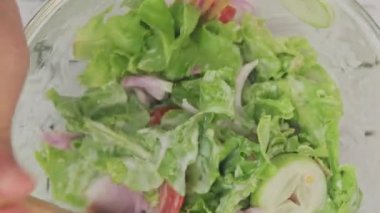 Mutfakta taze organik sebze salatası yapan bir kadın. Kadın elleri evde lezzetli sağlıklı yiyecekler hazırlıyor, bir kasede sebzeleri karıştırıyor, yakın plan.