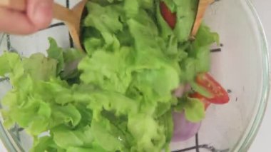 Mutfakta taze organik sebze salatası yapan bir kadın. Kadın elleri evde lezzetli sağlıklı yiyecekler hazırlıyor, bir kasede sebzeleri karıştırıyor, yakın plan.