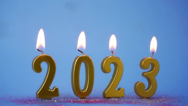 ホリデーバックグラウンド 新年2023年の黄金のライトナンバーキャンドルとハッピーニューイヤー 青い背景に金の燃えるろうそくによって作られる2023年の数 — ストック動画