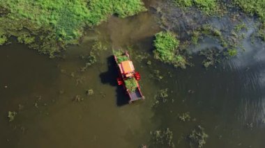 Büyük çelik bir gemide büyük bir kazıcı ve bir traktör kanalda çalışıyor sebze ve yabani otları topluyor..