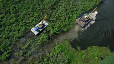 Büyük çelik bir gemide büyük bir kazıcı ve bir traktör kanalda çalışıyor sebze ve yabani otları topluyor..