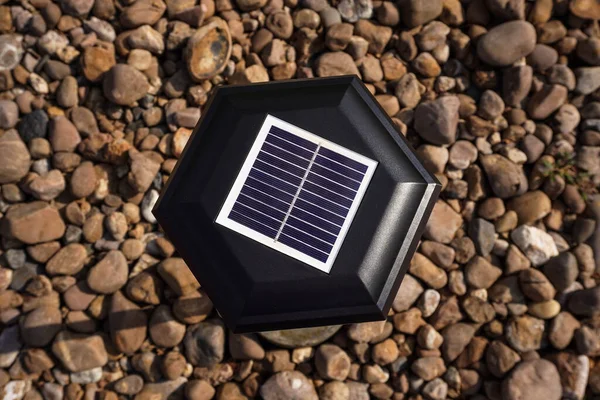 Small solar garden lights in the park. Solar powered lamp on pebbles background. Top view, selective focus on small solar panels on the lantern.