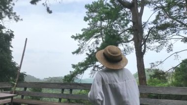 Asyalı bayan turist dışarıda, yemyeşil bir alanda bir parkta kamerayla fotoğraf çekiyor. Yaz turizmi kavramı.