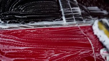 Kırmızı bir arabayı yıkayan ve oto yıkamada köpükle temizleyen birinin yakın çekimi..