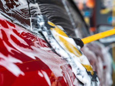 Kırmızı bir arabayı yıkayan ve oto yıkamada köpükle temizleyen birinin yakın çekimi..