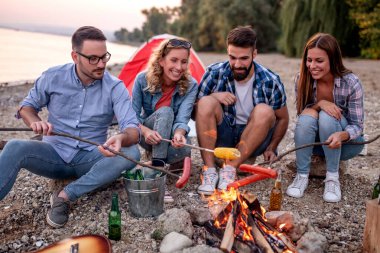 Genç bir arkadaş grubu sosis ızgara yapıyor. Açık hava, ızgara, arkadaşlar, insanlar ve yaşam tarzı konsepti..