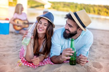 Genç çift sahilde eğleniyor, bira içiyor ve gülümsüyor..
