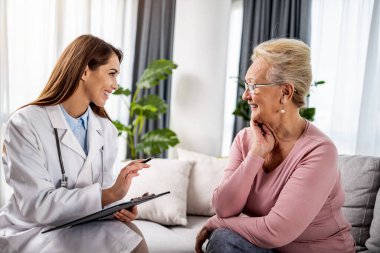 Ev ziyareti sırasında kıdemli hastaya yardımcı olan kadın doktor. Doktor, yaşlı kadınla koronavirüs salgınını tartışıyor..