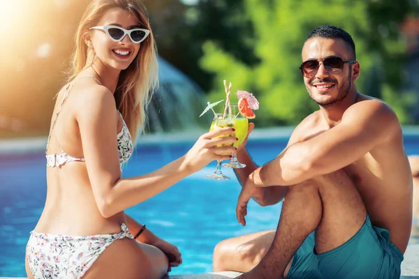 Young couple drinking cocktail by the swimming pool.