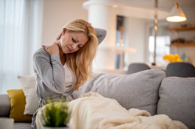 Sick woman with back pain sitting on a sofa at home. People,medicine, healthcare and home concept.
