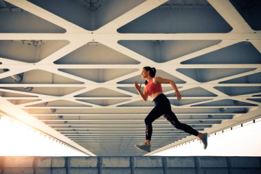 Young fitness woman running on city bridge. Modern exterior.