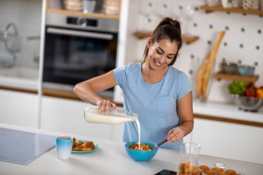 Portrait of beautiful young woman having breakfast in the kitchen.She is eating cornflakes.