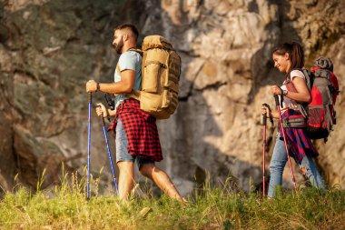 Hikers with backpacks and hiking sticks walking through forest together. clipart