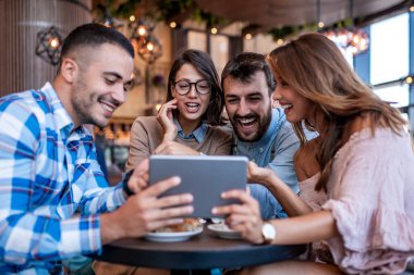Group of four friends having a coffee together. Two women and two men enjoying their time, using digital tablet.