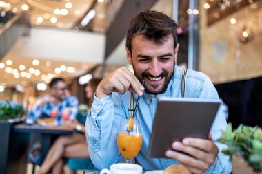 Leisure time. Young attractive man looking at tablet while drink juice and coffee.
