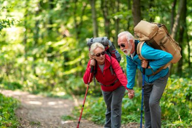 Aktif kıdemli çift sırt çantalarıyla ormanda yürüyüş yapıyor, maceralarının tadını çıkarıyorlar..