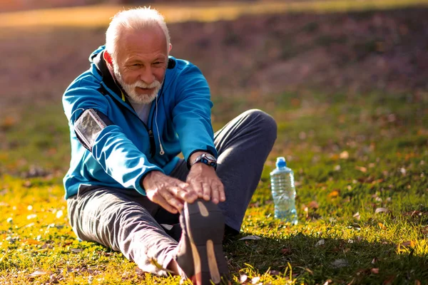 Portrait of happy senior man in sportswear stretching in the park.