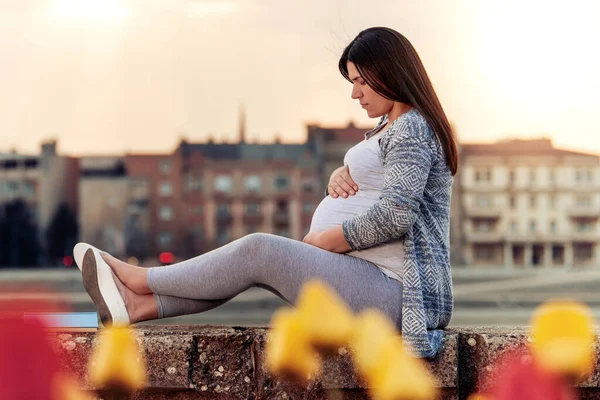 屋外に座って腹に触れる妊娠中の女性 — ストック写真